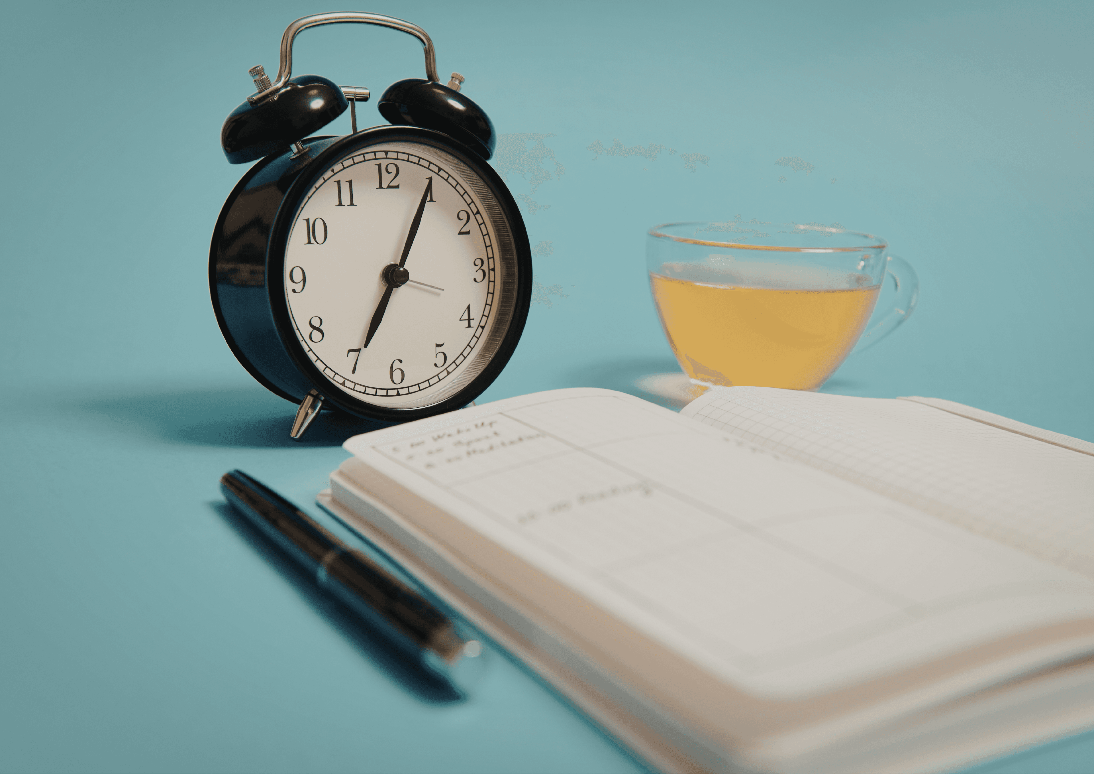 Ein Wecker, ein Heft, ein Schreibstift und eine Tasse Tee stehen auf einem türkisfarbenen Untergrund