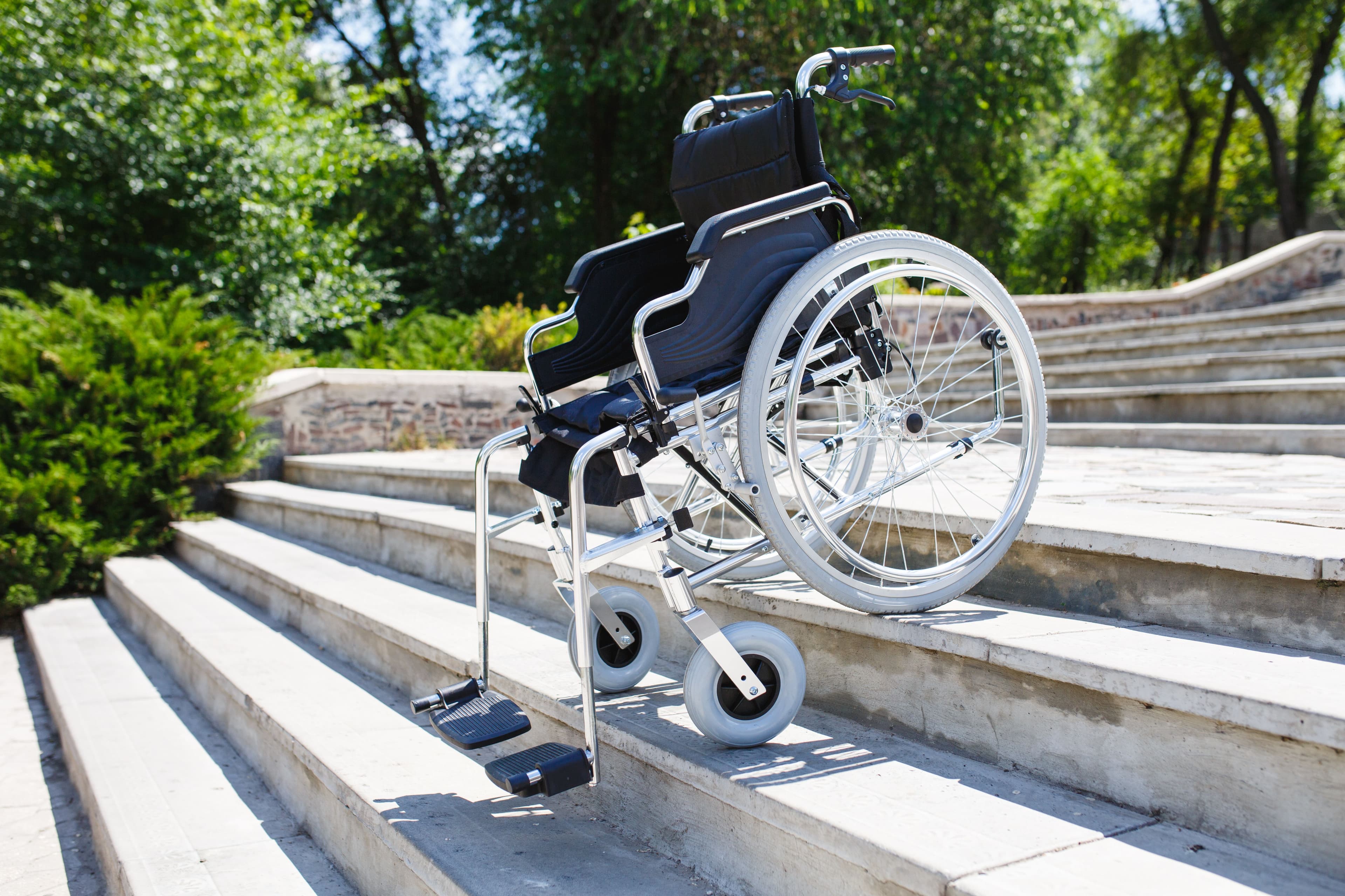 Leerer Rollstuhl der abwärtsschauend und schief geneigt auf einer Treppe steht.