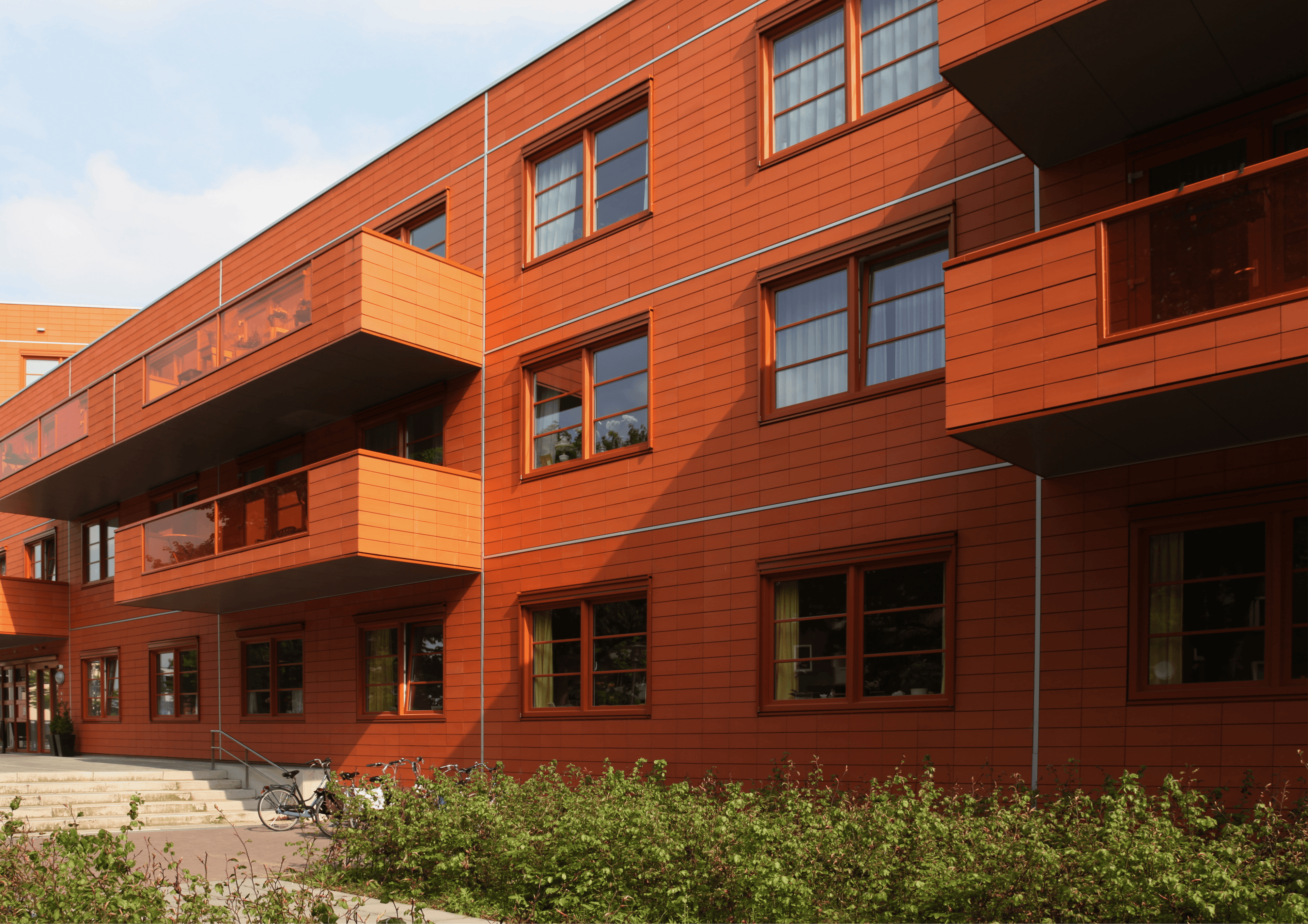 Wohngebäude von aussen mit rost-roter Fassade und Balkonen.