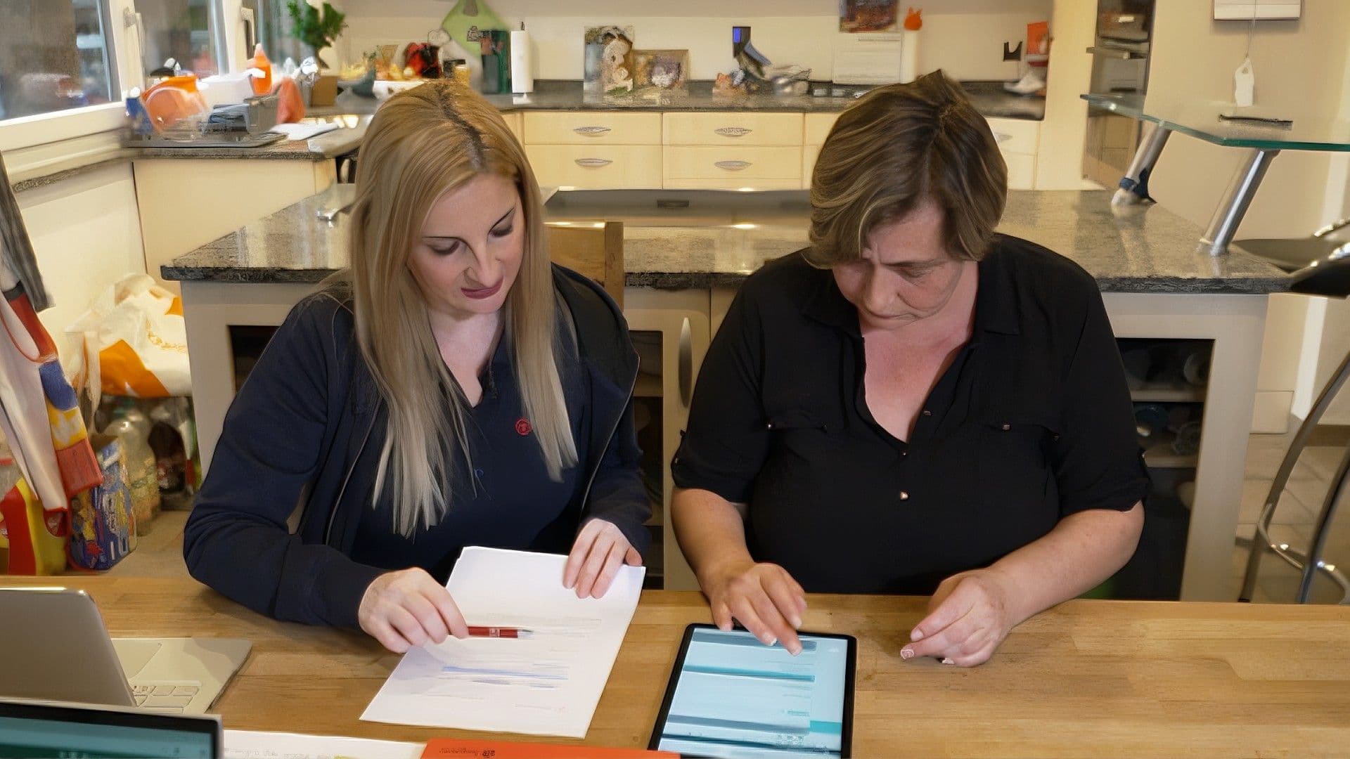 Zwei Frauen sitzen am Tisch und besprechen etwas, beide schauen dabei auf das vor ihnen liegende Papier.