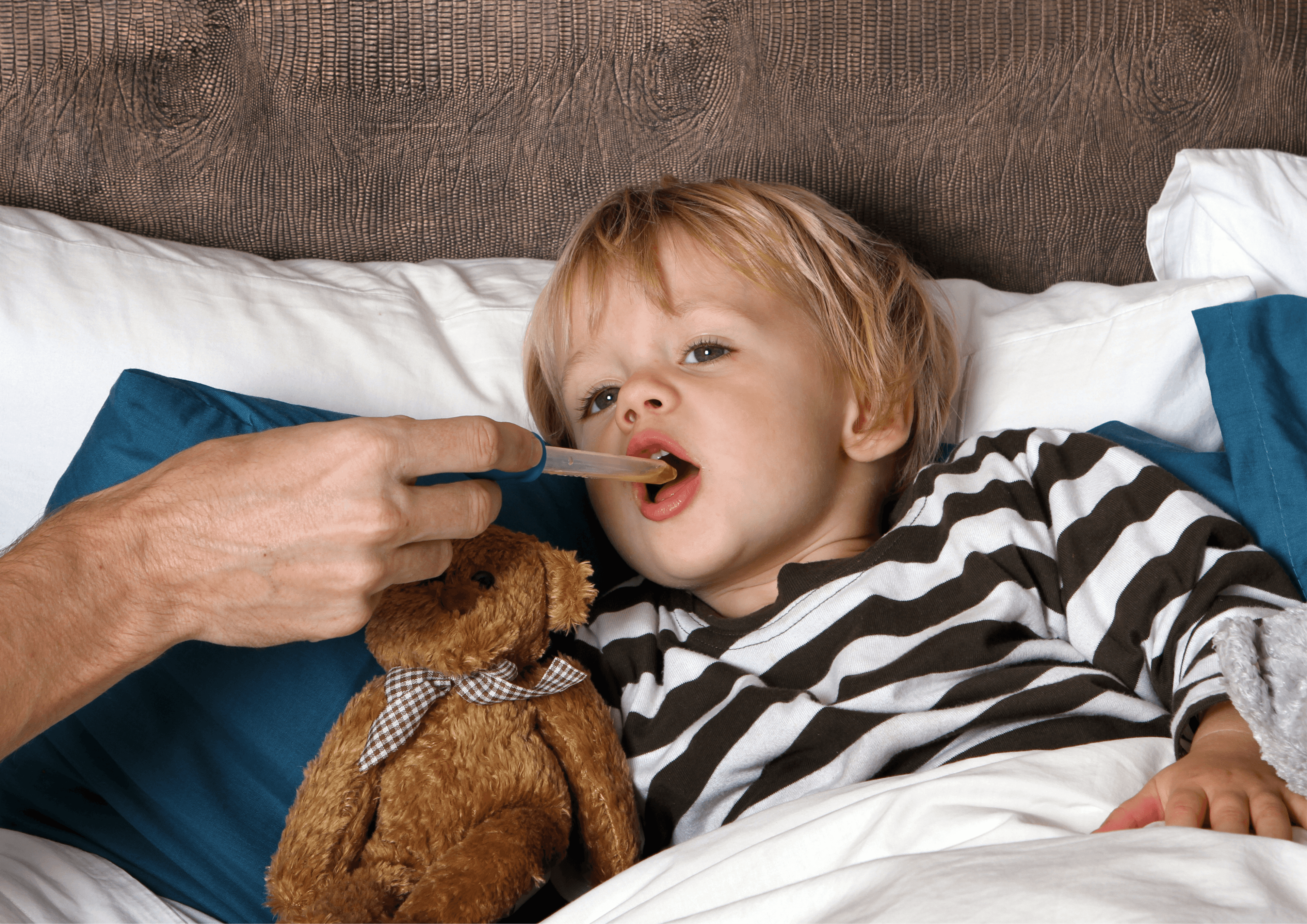 Kind im liegt im Bett und es wird ihm mit einer Pipette eine Flüssigkeit in den Mund gegeben.