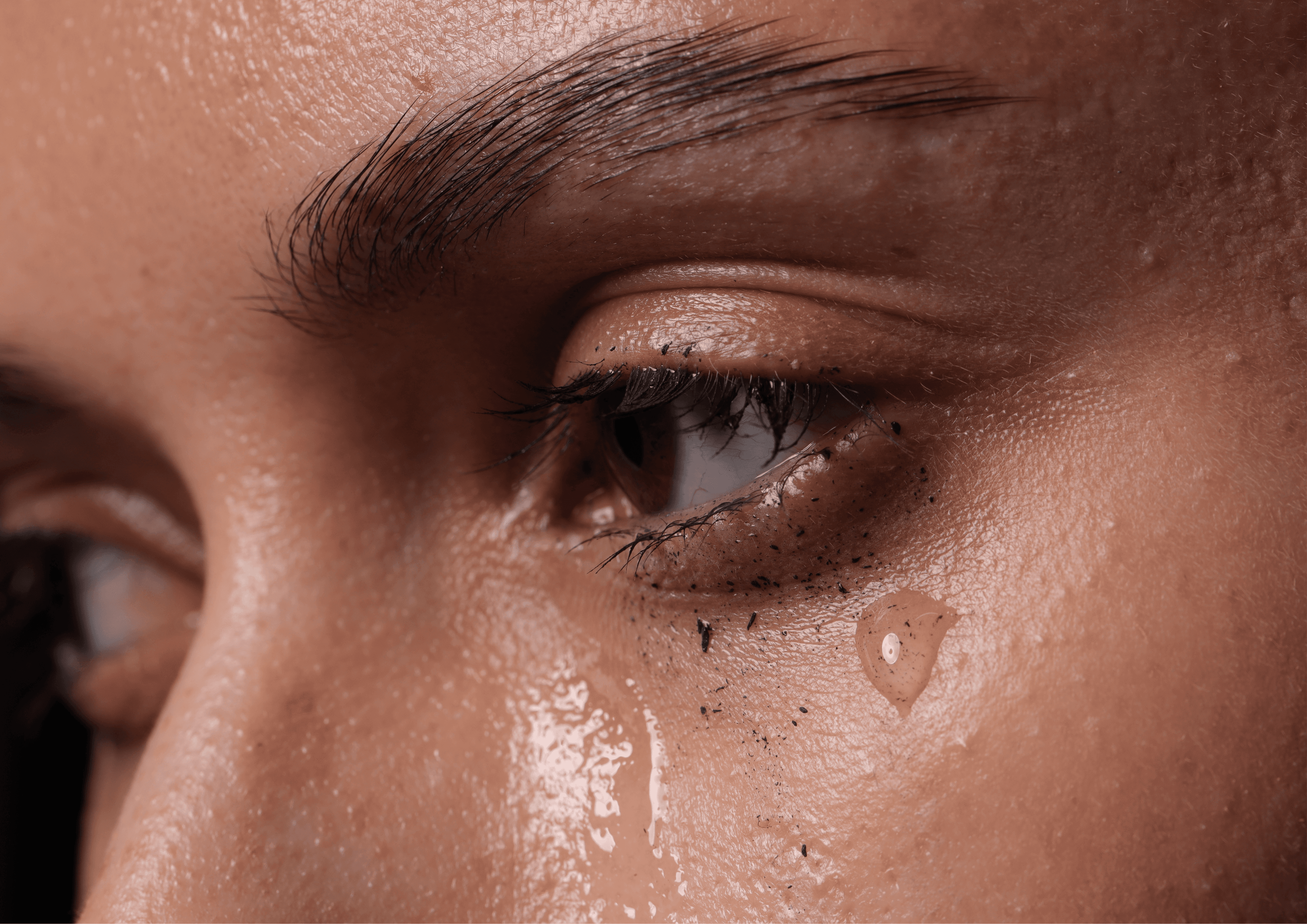 Fotoausschnitt bei welchem man nur die Augen leicht seitlich sieht, die Frau hat Tränen in den Augen und die Wimperntusche ist leicht abgerieben.