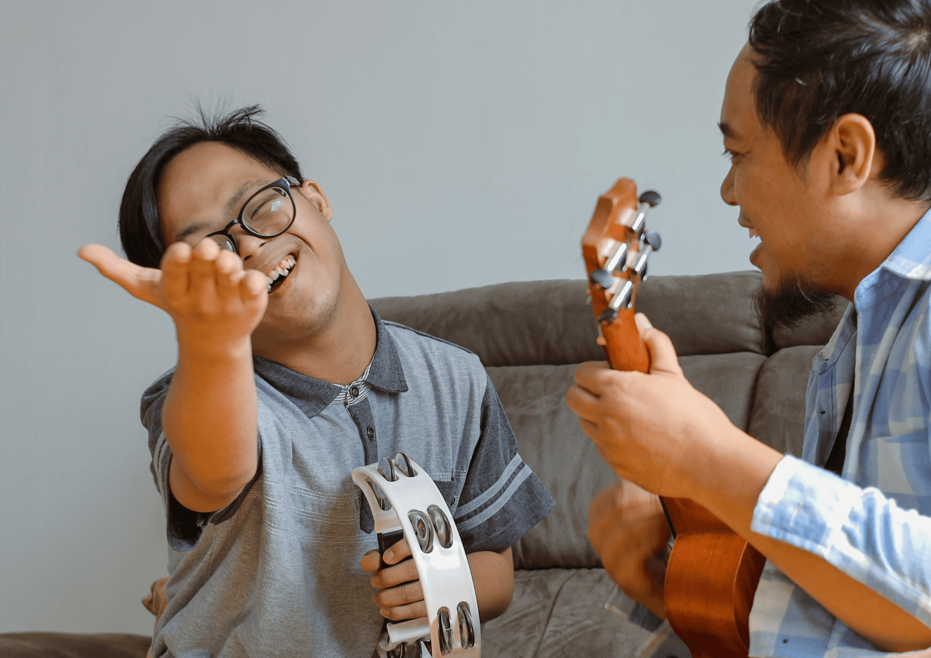 Zwei Menschen mit Musikinstrumenten in der Hand auf einem Sofa, einer lacht in die Kamera.