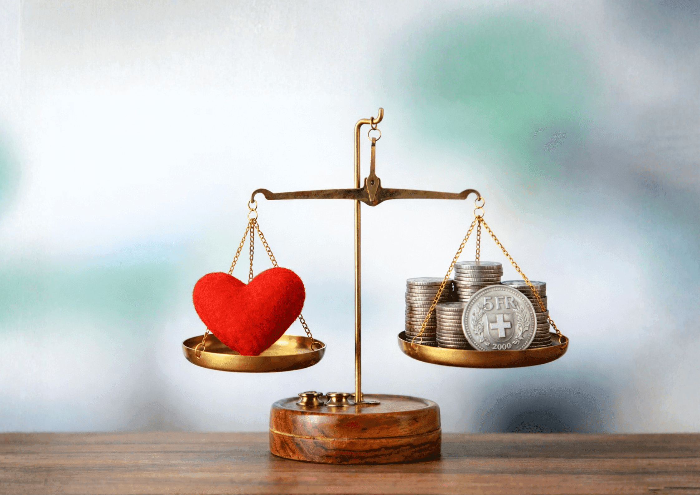 Waage mit Waagschalen in welchen sich ein Herz auf der linken Seite und Münzen auf der Rechten Seite ausbalancieren.